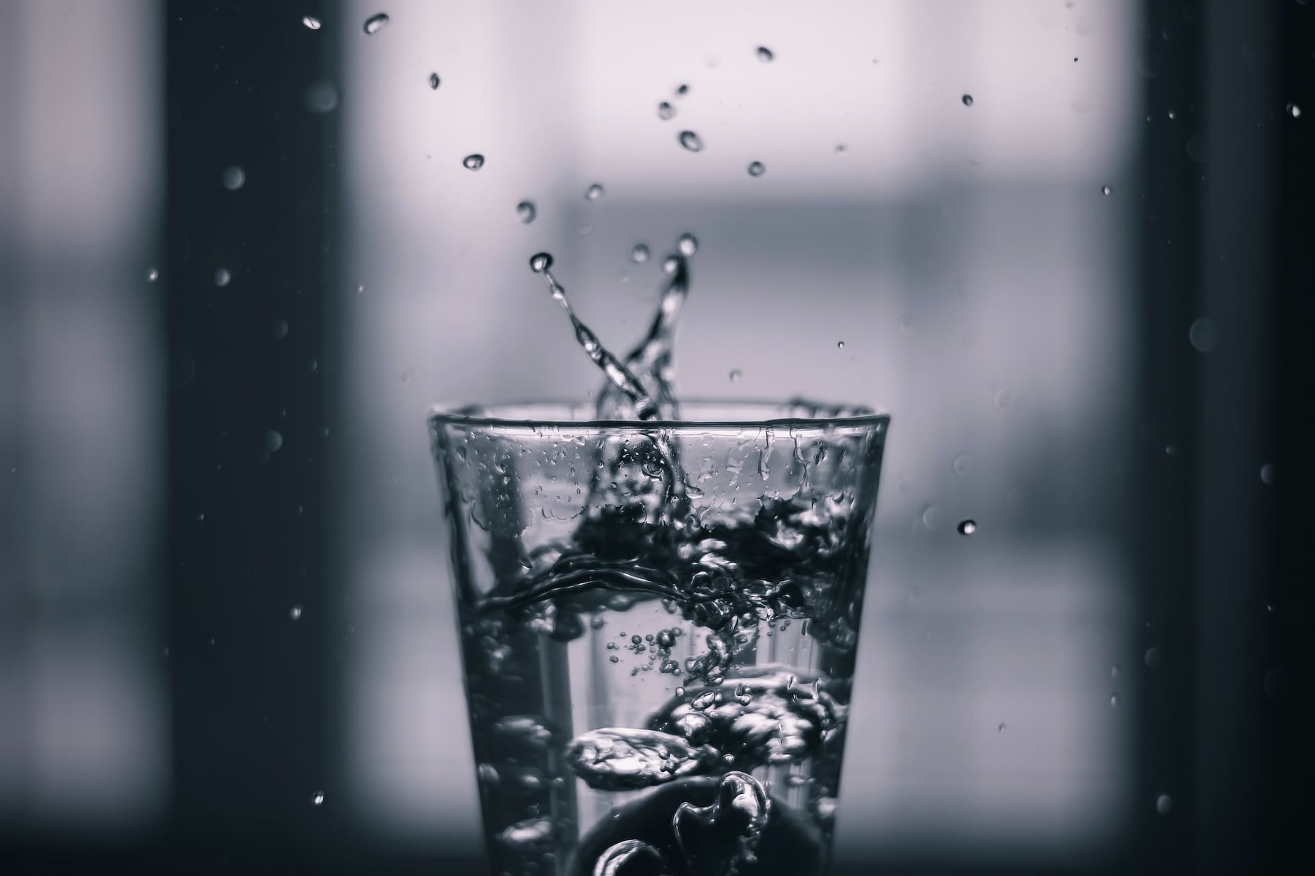 A close-up of a kitchen faucet, where the water flow is weak and sputtering. Below, a glass collects the water, revealing a slightly cloudy appearance with minuscule particles suspended.