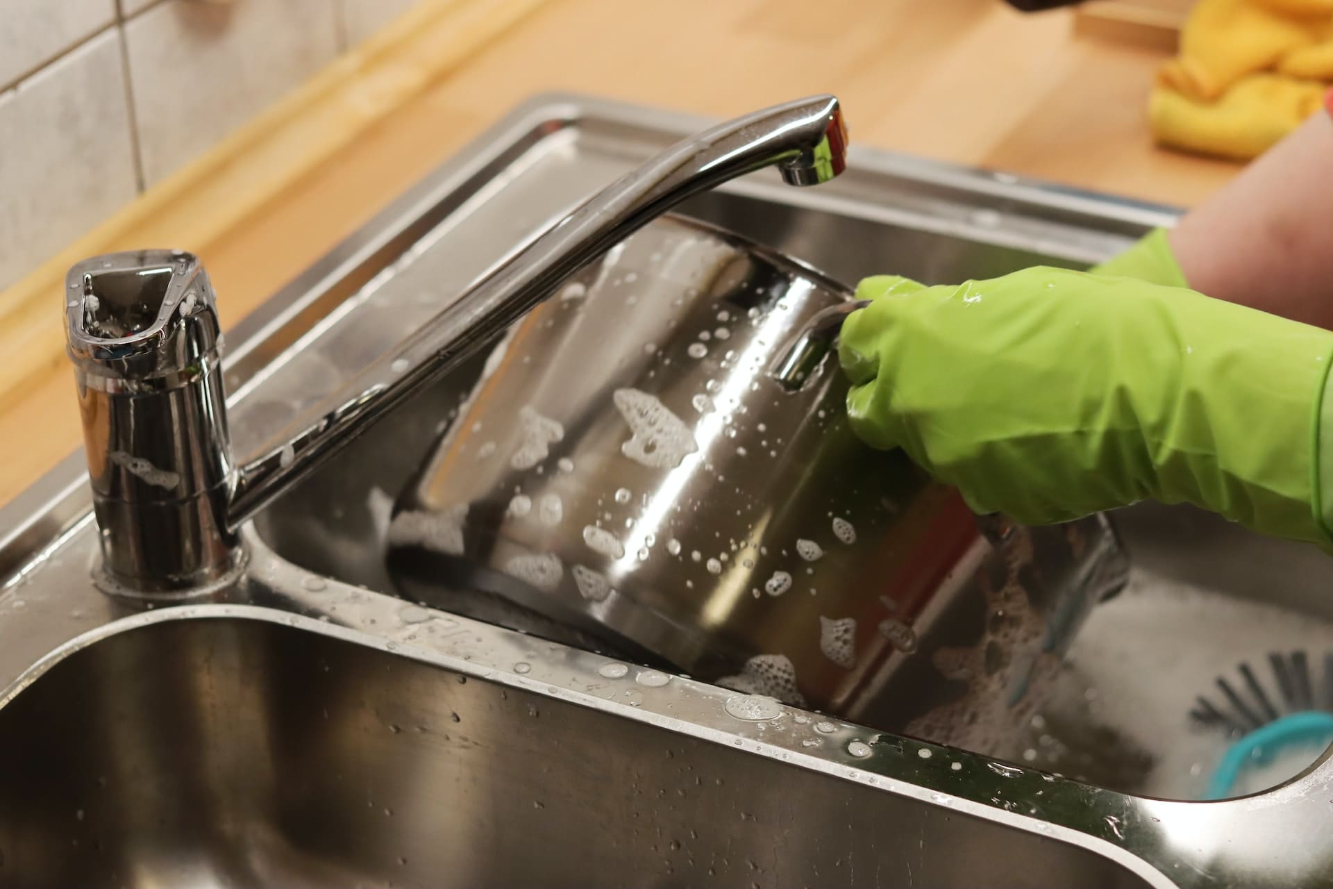 A close-up of a clear glass on a kitchen countertop, filled with water that has a faint greenish hue. Nearby, a dropper dispenses a single drop into the glass, suggesting a test or additive.
