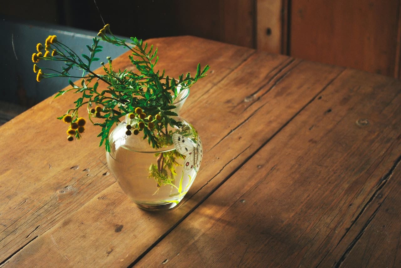 A close-up of a glass filled with water on a balcony table. The water has a faint greenish hue, and a leaf with a few spots floats on the surface.