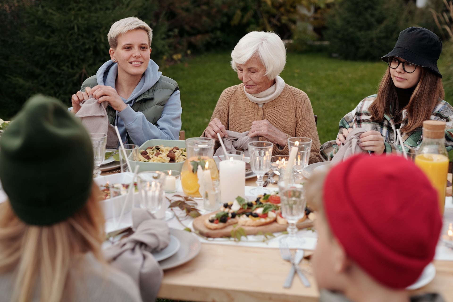 A backyard scene with a wooden deck. Friends gather for a barbecue, laughing and chatting, with a pitcher of clear water adorned with citrus slices and ice cubes at the center of the table.