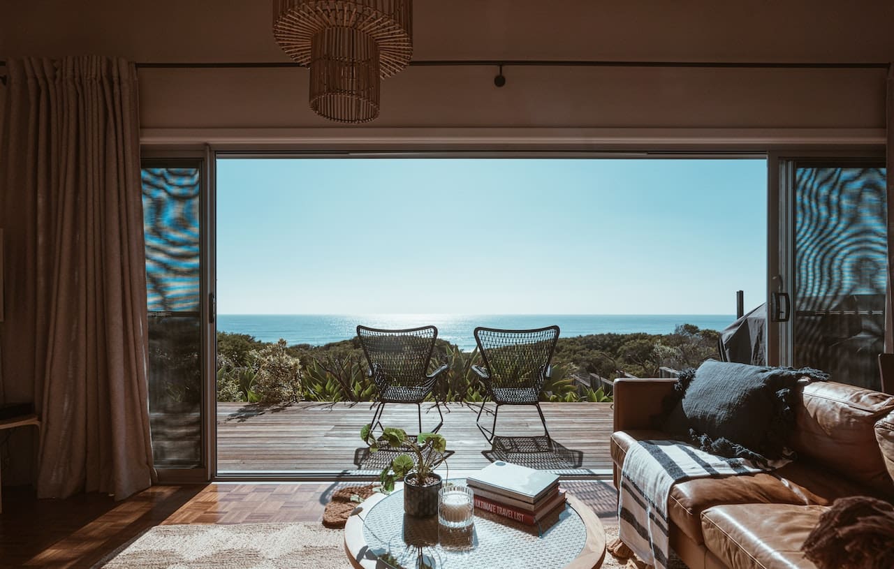 A sunlit balcony overlooking the ocean. A couple relaxes in lounge chairs, sipping from tall glasses filled with sparkling water, ice cubes, and lime wedges.