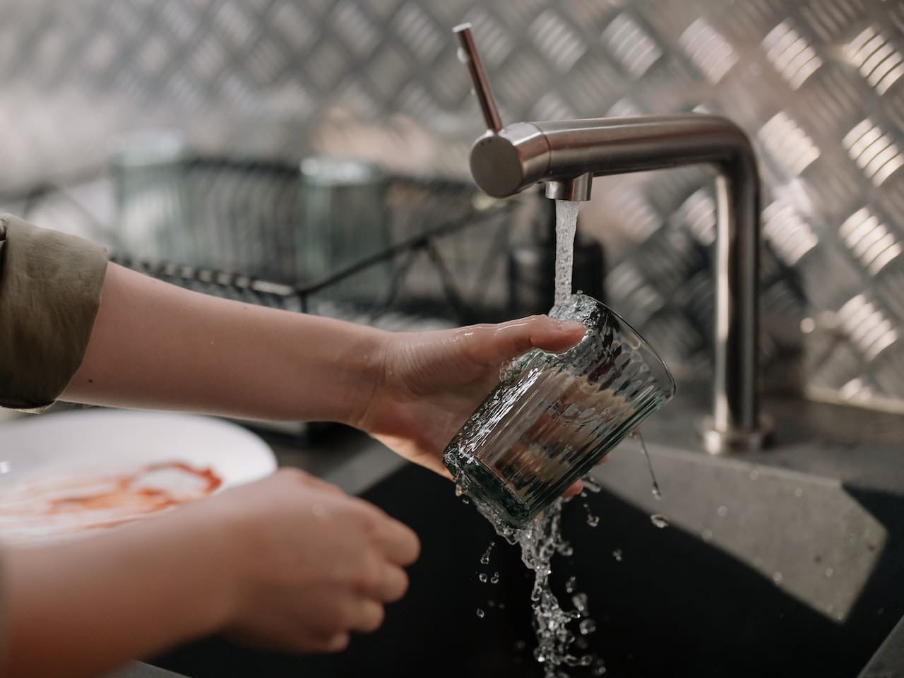 A photo-realistic image of a contemporary kitchen, where a family is gathered around a water filtration system, filling their glasses with clear, purified water from the tap.