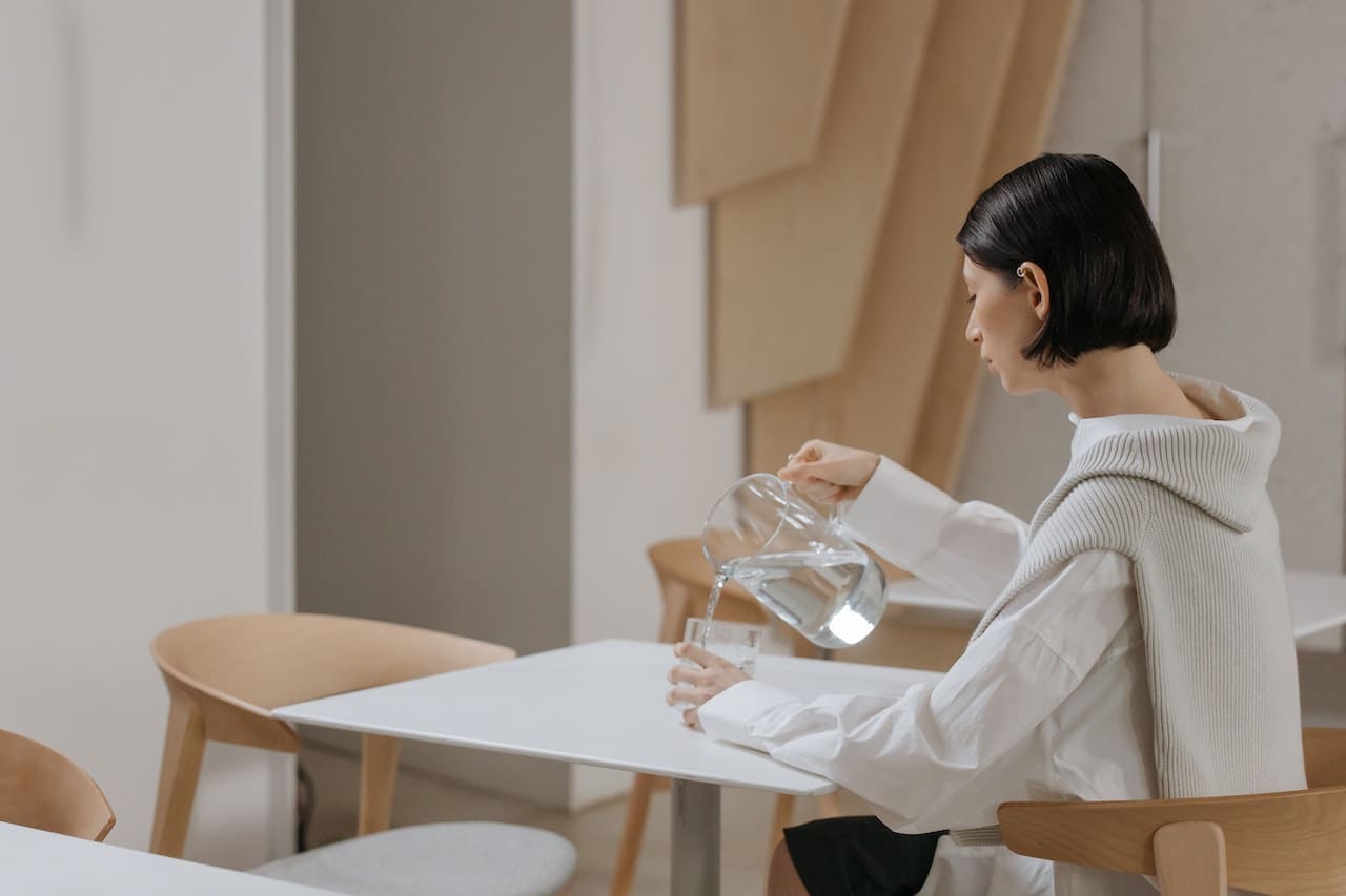 An image of a homeowner pouring a glass of water from a pitcher in the kitchen with a noticeable odor and taste, highlighting concerns about the quality of drinking water in The Woodlands.