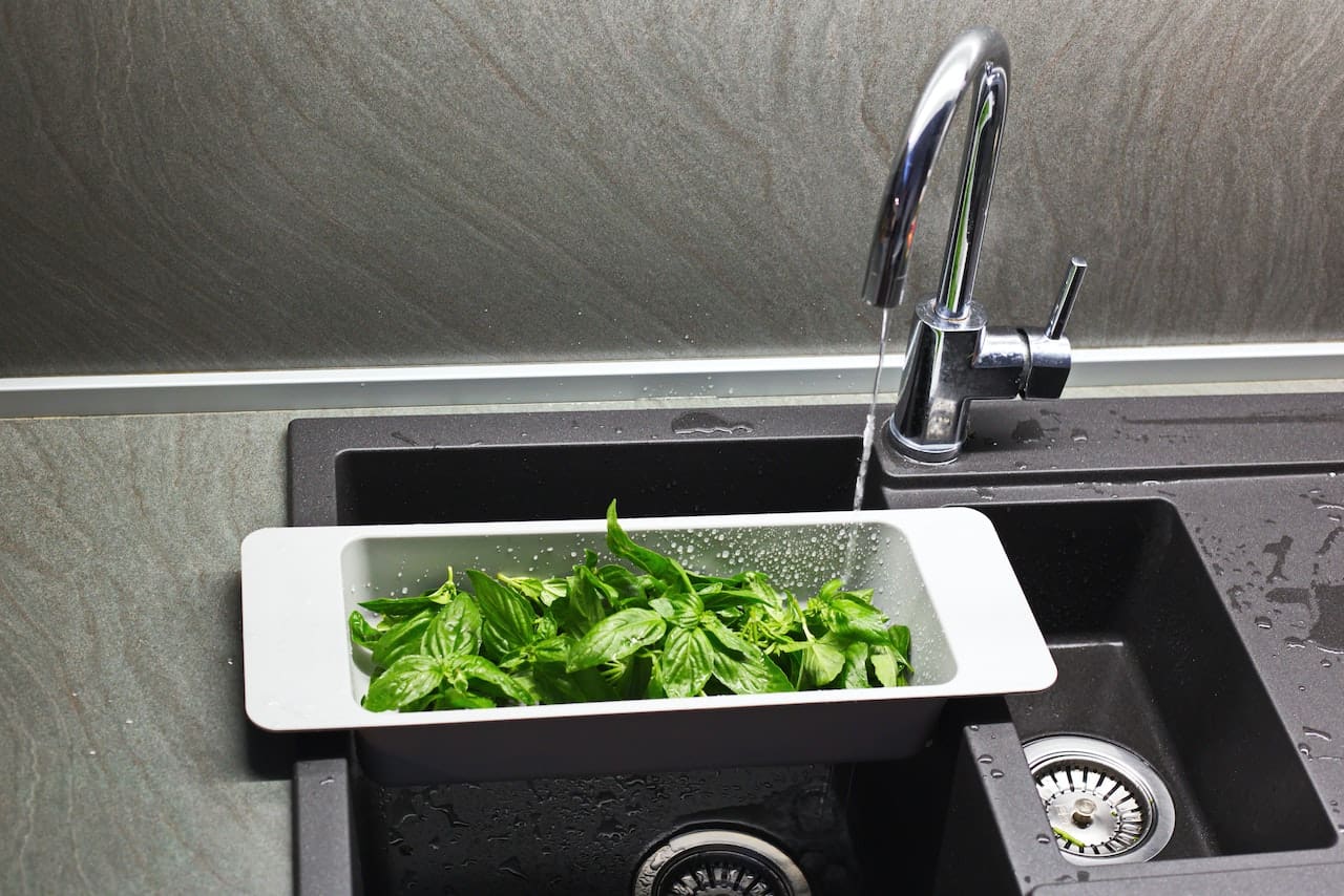 A close-up of a kitchen sink with water flowing, but the stream is interrupted by occasional air bubbles. The surrounding stainless steel shows faint water streaks and mineral deposits.
