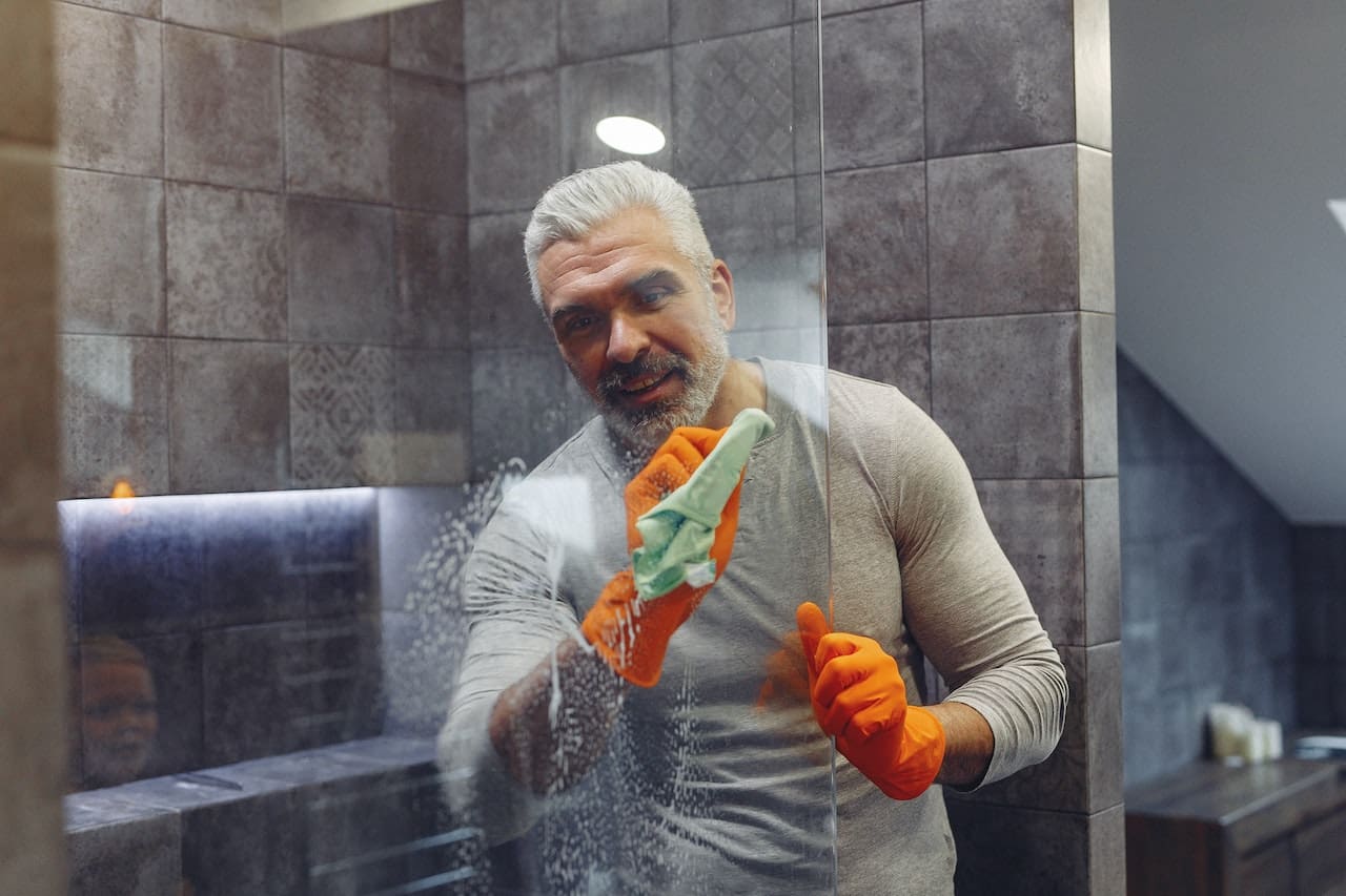 An image of a resident scrubbing away hard water stains on a shower door, illustrating the challenges of water quality in San Antonio households.