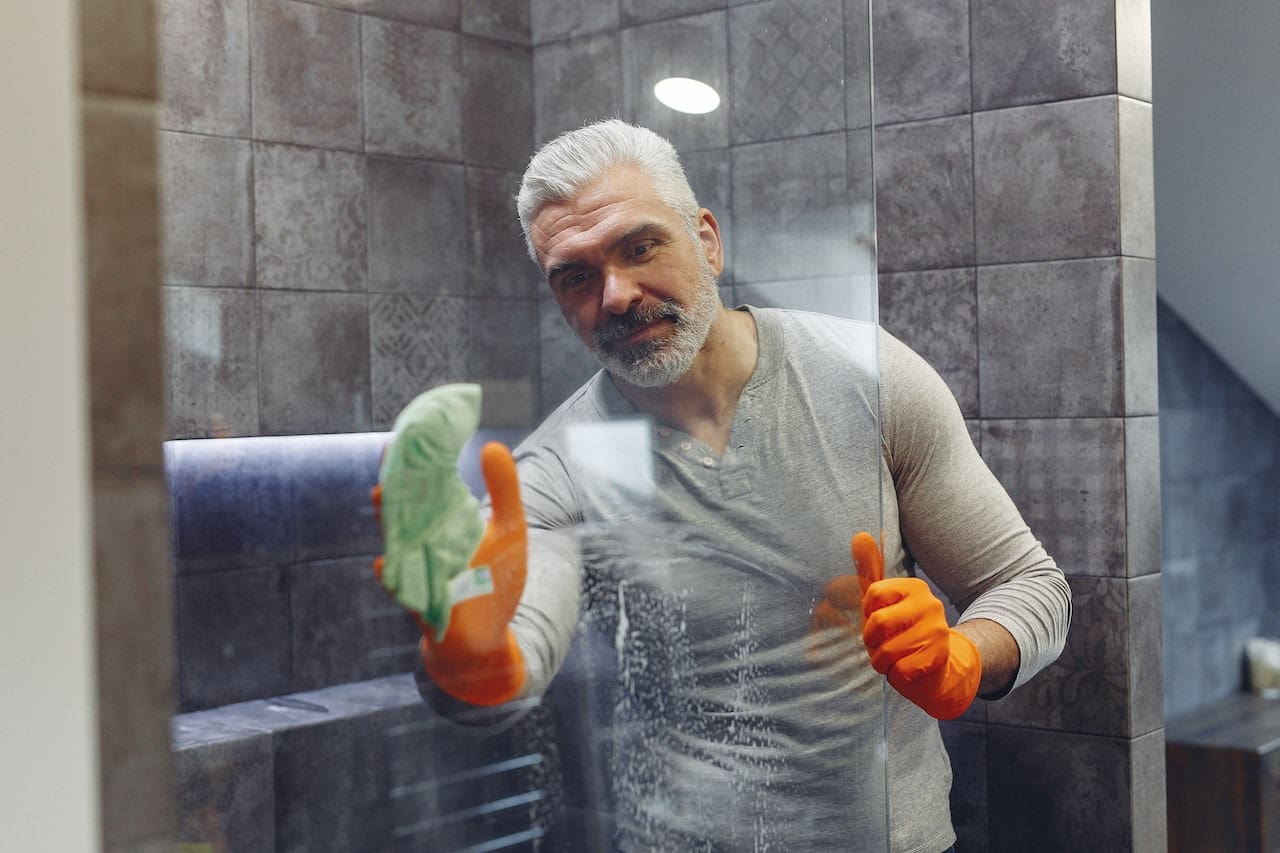 An image of a homeowner scrubbing away hard water stains on a shower door, illustrating the challenges of water quality in McAllen households.