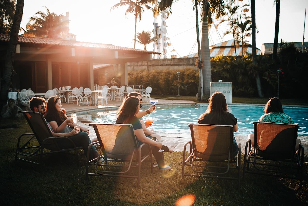 A heartwarming snapshot of friends gathering in a backyard with a pristine swimming pool, enjoying a sunny day and cool refreshments, illustrating the pleasures of outdoor living in Frisco.