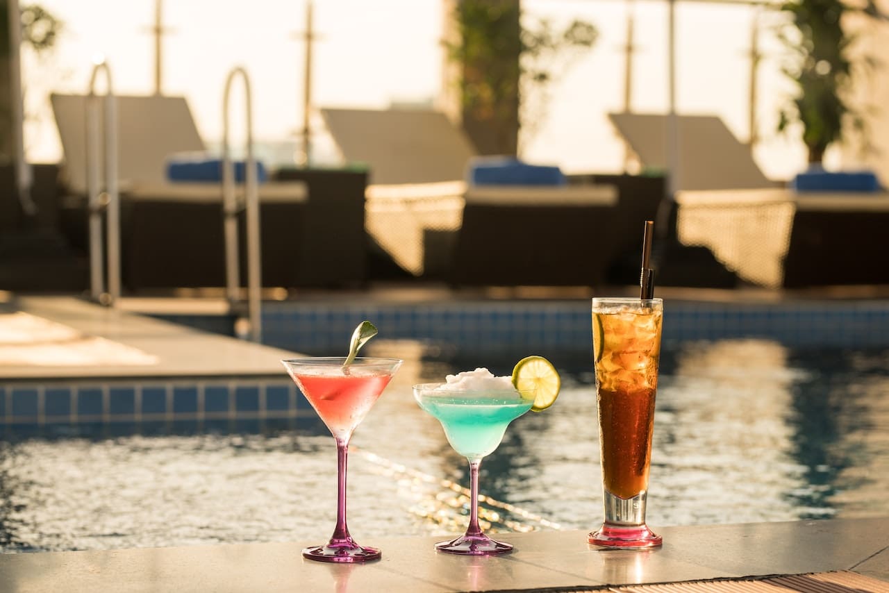 A Couple Relaxes In Lounge Chairs, Sipping From Tall Glasses Filled With Sparkling Water, Ice Cubes, And Lime Wedges.