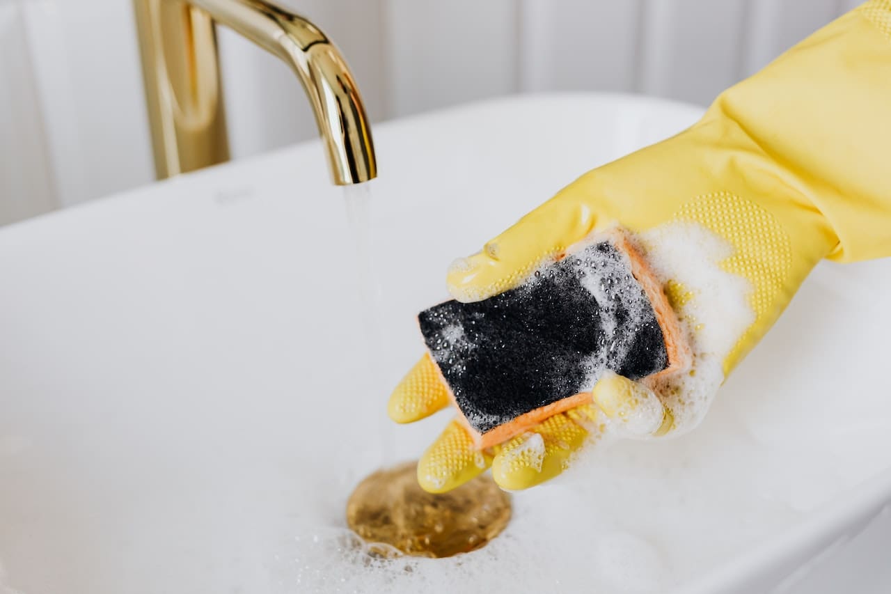 A close-up of a bathroom sink faucet with water flowing, but the stream is inconsistent, alternating between strong and weak flows. The surrounding porcelain sink shows faint rust-colored stains near the drain.