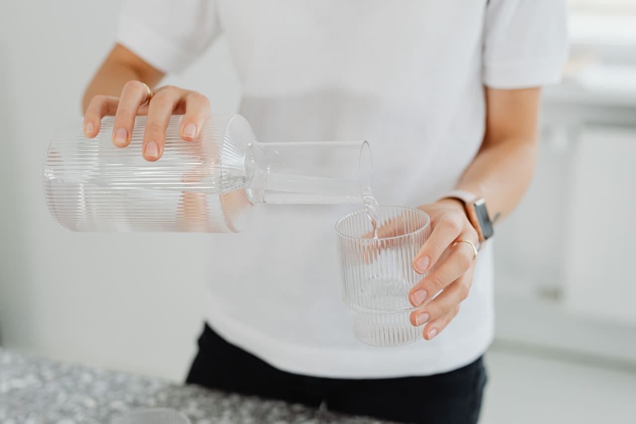 A picture of a homeowner pouring a glass of discolored tap water, with a kid looking in the background, highlighting concerns about water quality in some parts of Carrollton.