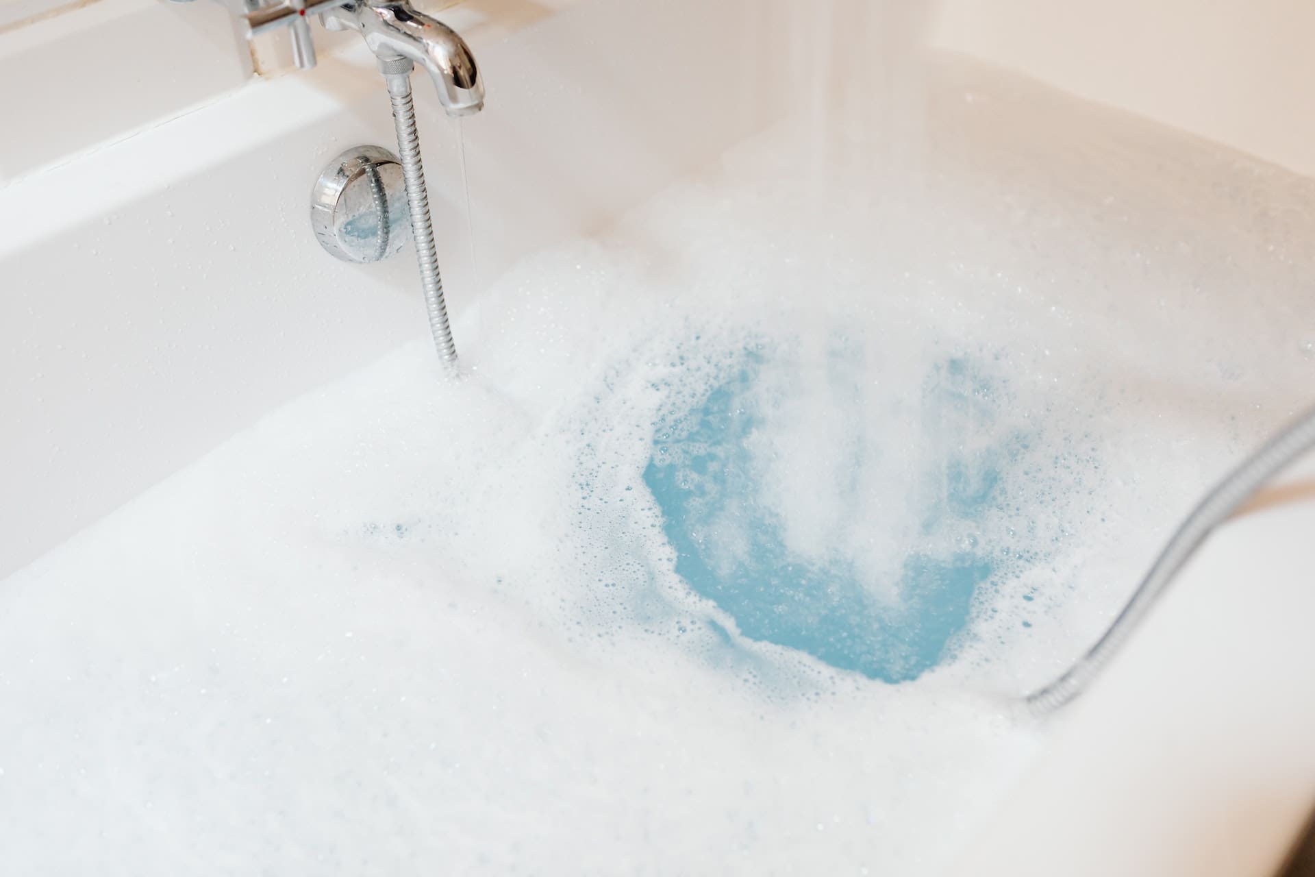 A bathroom scene with a filled bathtub. On the water's surface, there's a thin film, and the water appears slightly murky, with a few bubbles rising.