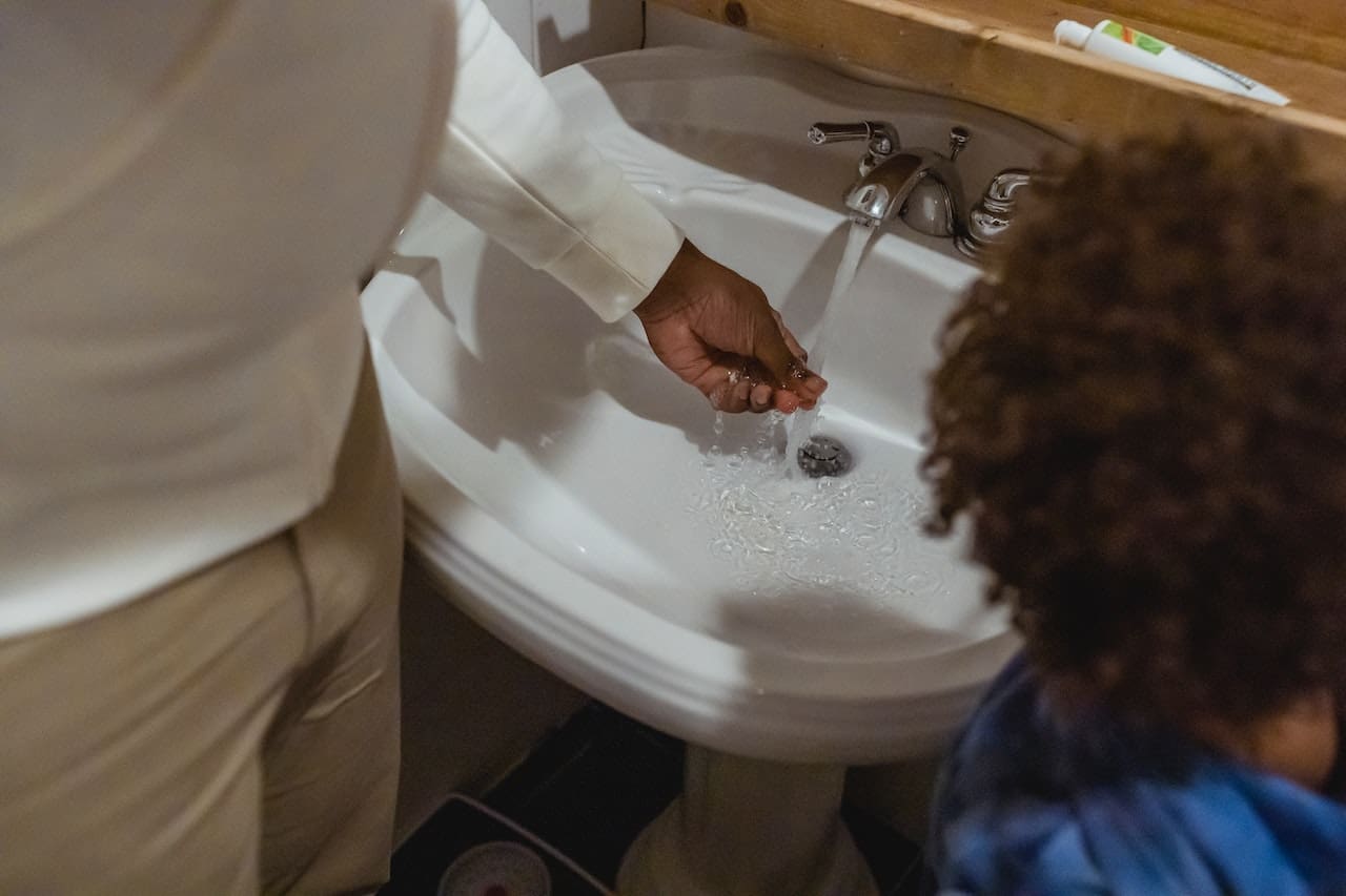 A picture of a homemaker scrubbing away hard water stains on dishes with children watching over in convern caused by unfiltered water, highlighting the need for clean water for daily use in Laredo households.