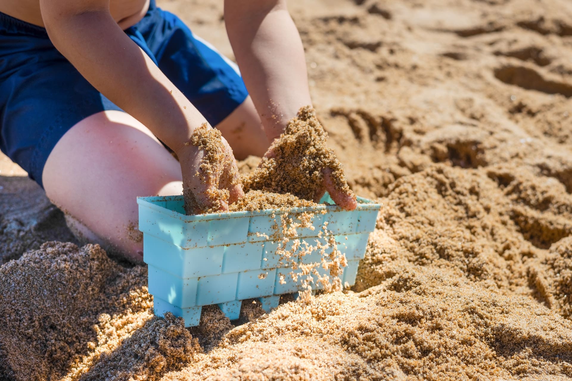 A close-up of a beachgoer's hand scooping up a handful of sand, revealing tiny bits of microplastics and debris mixed in with the grains.