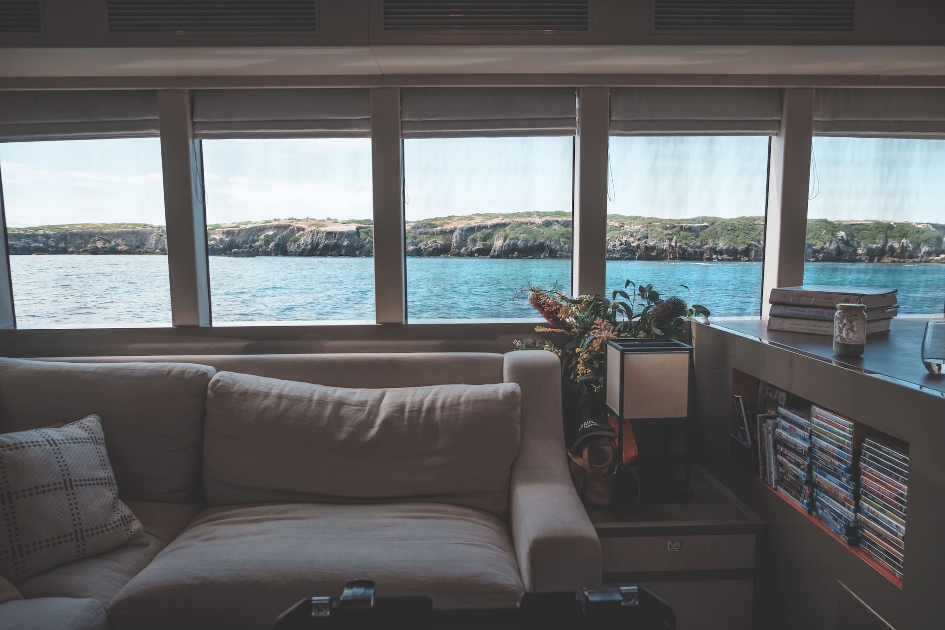 A modern condo interior with floor-to-ceiling windows offering panoramic ocean views. A group of friends toast with tall glasses filled with sparkling water, ice cubes, and fresh fruit garnishes.