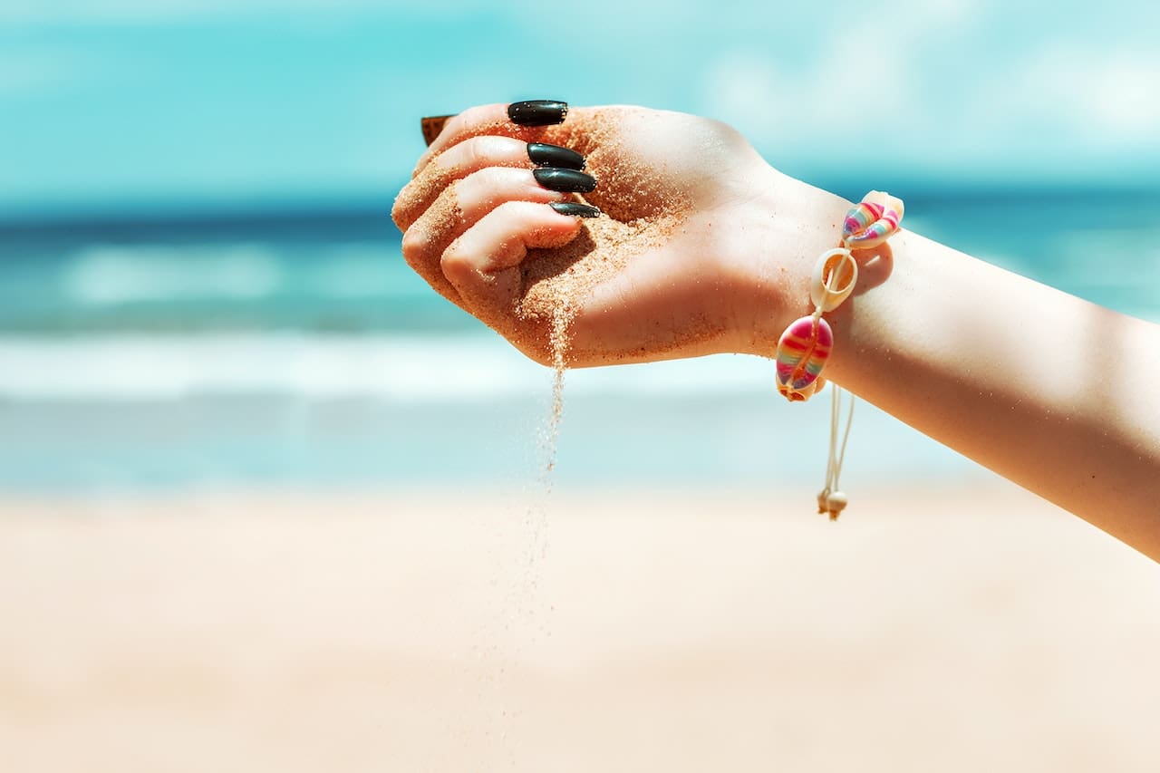 A close-up of a beachgoer's hand scooping up a handful of sand, revealing tiny bits of microplastics and debris mixed in, symbolizing pollution and contamination.