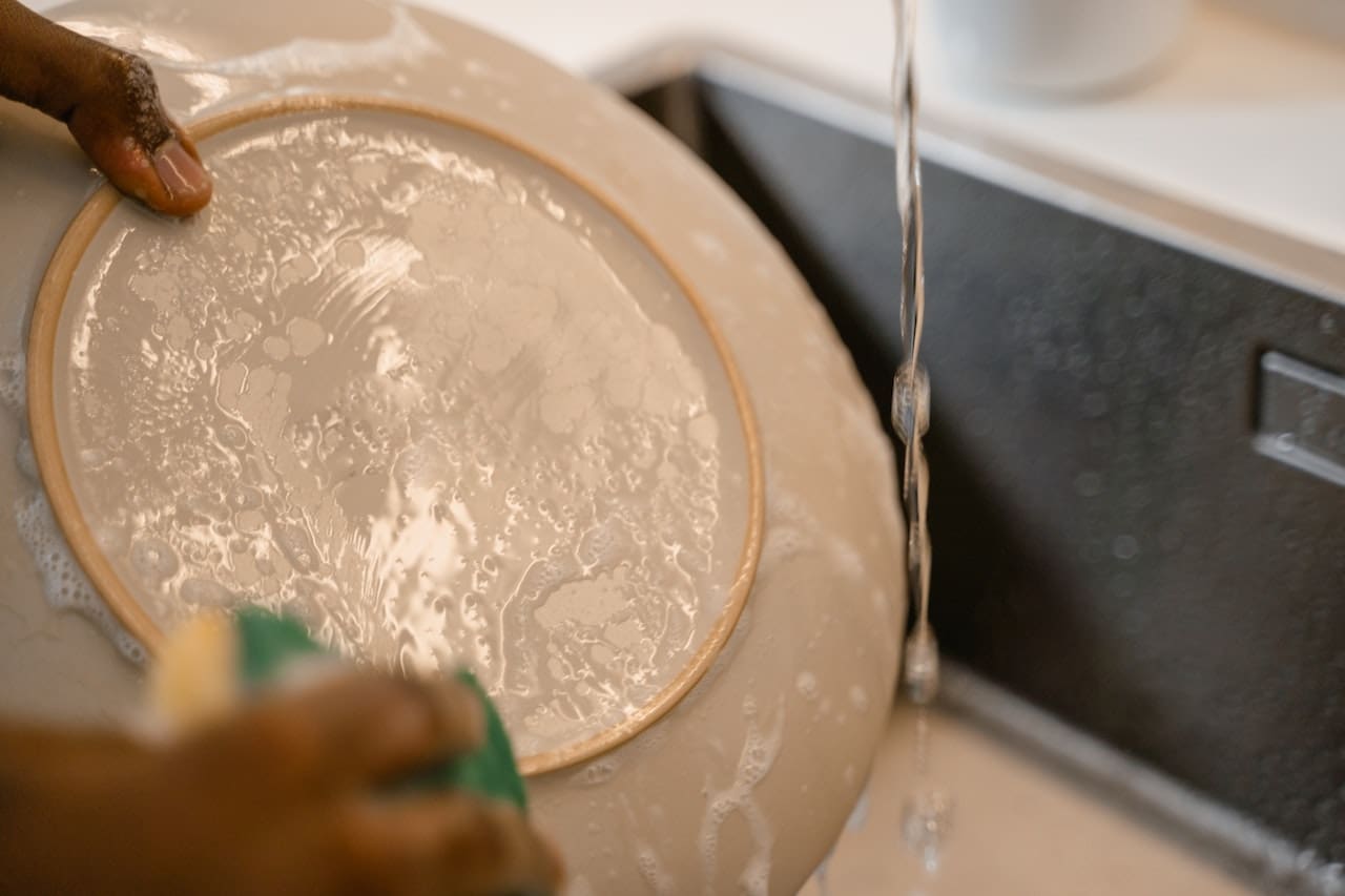 An image of a homeowner scrubbing away stains on dishes caused by unfiltered water, highlighting the importance of clean water for cooking and dishwashing in Temple households.