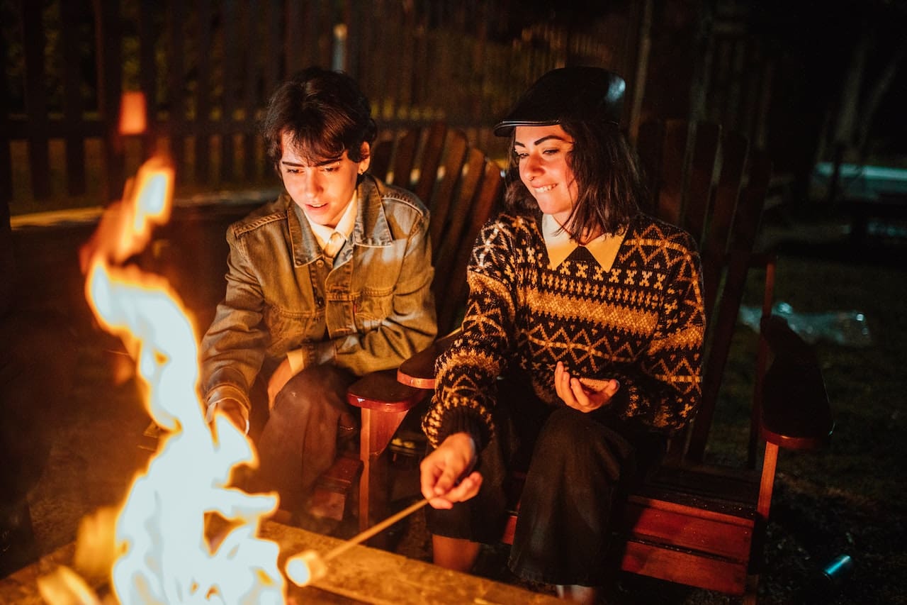 A cozy evening scene of friends gathered around a fire pit in their backyard, enjoying roasted marshmallows and warm beverages made with pure water, exemplifying the pleasures of outdoor leisure in League City.