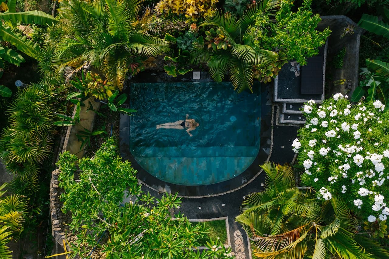 A photo-realistic image of a backyard oasis, where a family lounges by a swimming pool, and a garden hose waters the colorful flowerbeds.