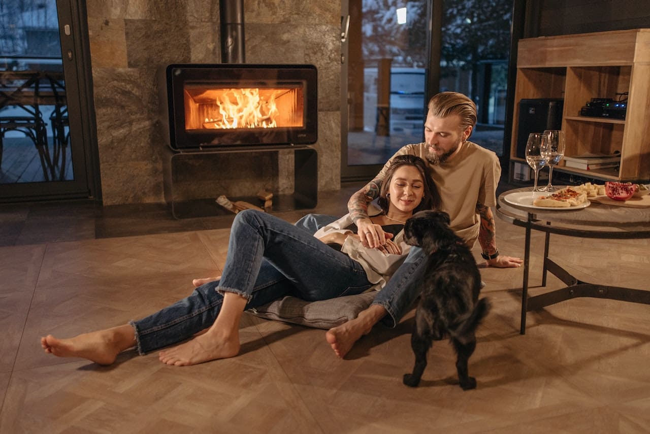 A photo-realistic image of a cozy living room with a fireplace, where a couple sips on warm mugs of tea brewed with filtered water.