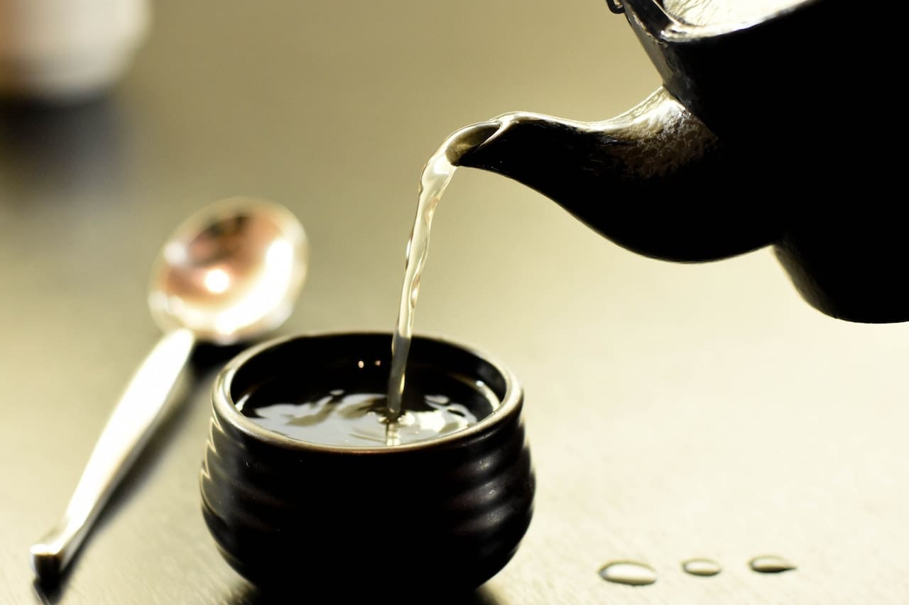 A close-up of a kitchen faucet with water flowing, but the stream has a slight brownish tint. Nearby, a coffee mug shows faint water stains on its interior.