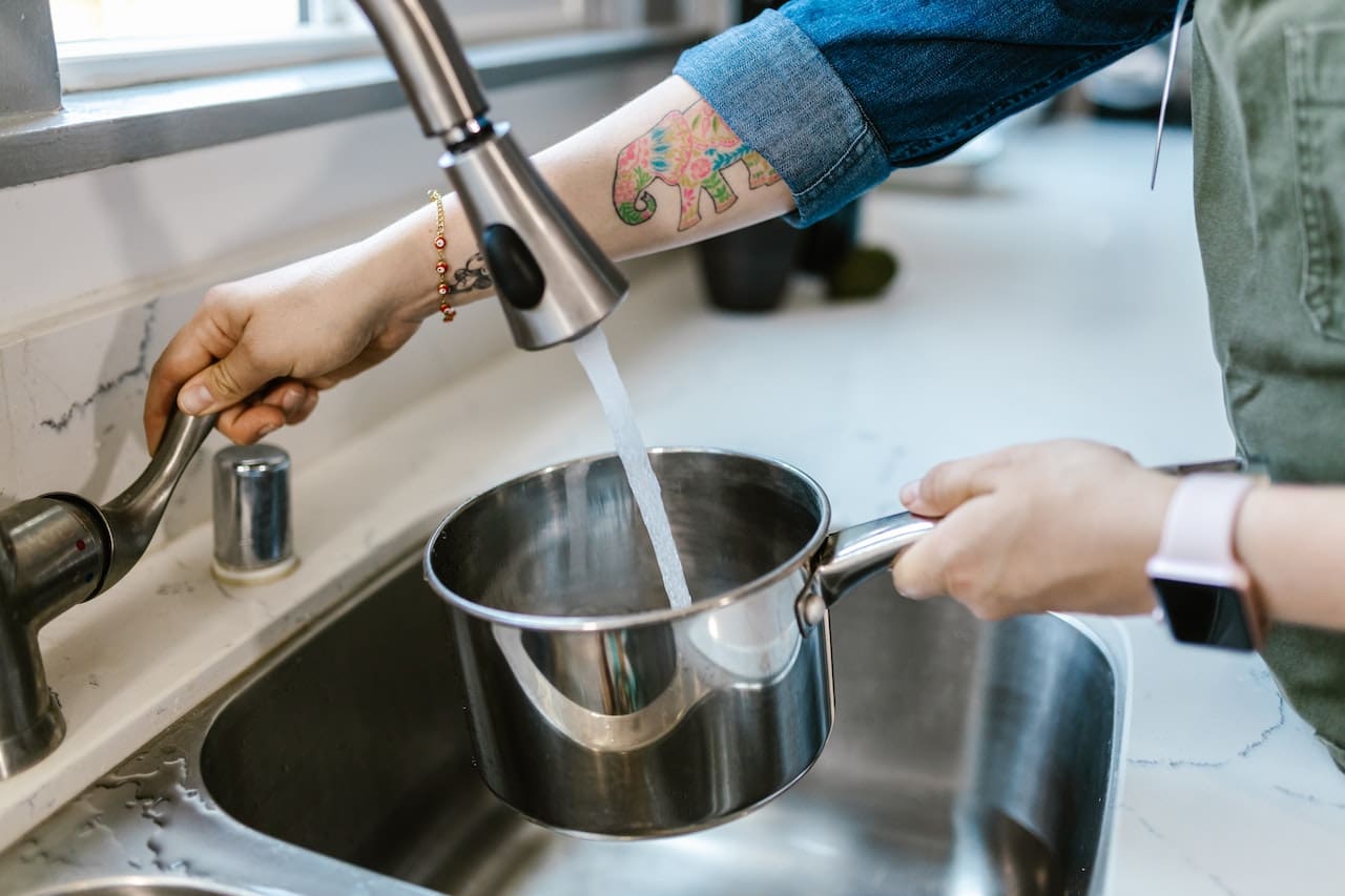 An image of a homeowner pouring cloudy tap water into a pot for cooking, emphasizing the importance of filtered water in Richardson kitchens.