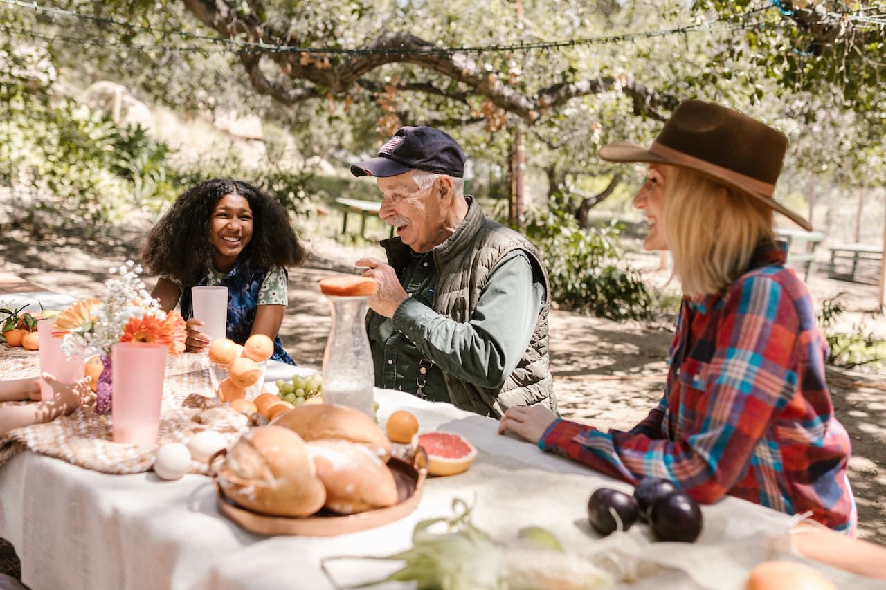 A photo-realistic image of a family enjoying a country-style picnic under the shade of a tree, with glasses of fresh well water, highlighting the simplicity and joys of rural life.