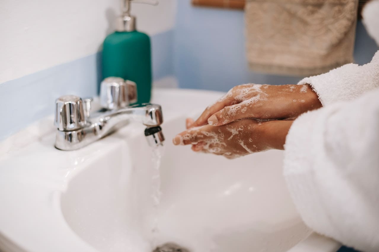 A bathroom sink faucet with water flowing, but the stream has a slight brownish tint. The surrounding porcelain sink shows faint rust-colored stains near the drain.
