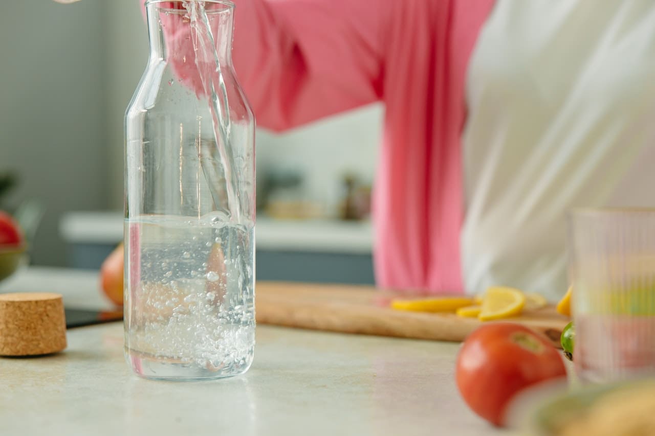 An image of a man pouring a glass of discolored tap water, in front of the television in the living room highlighting concerns about water quality in some parts of Denton.