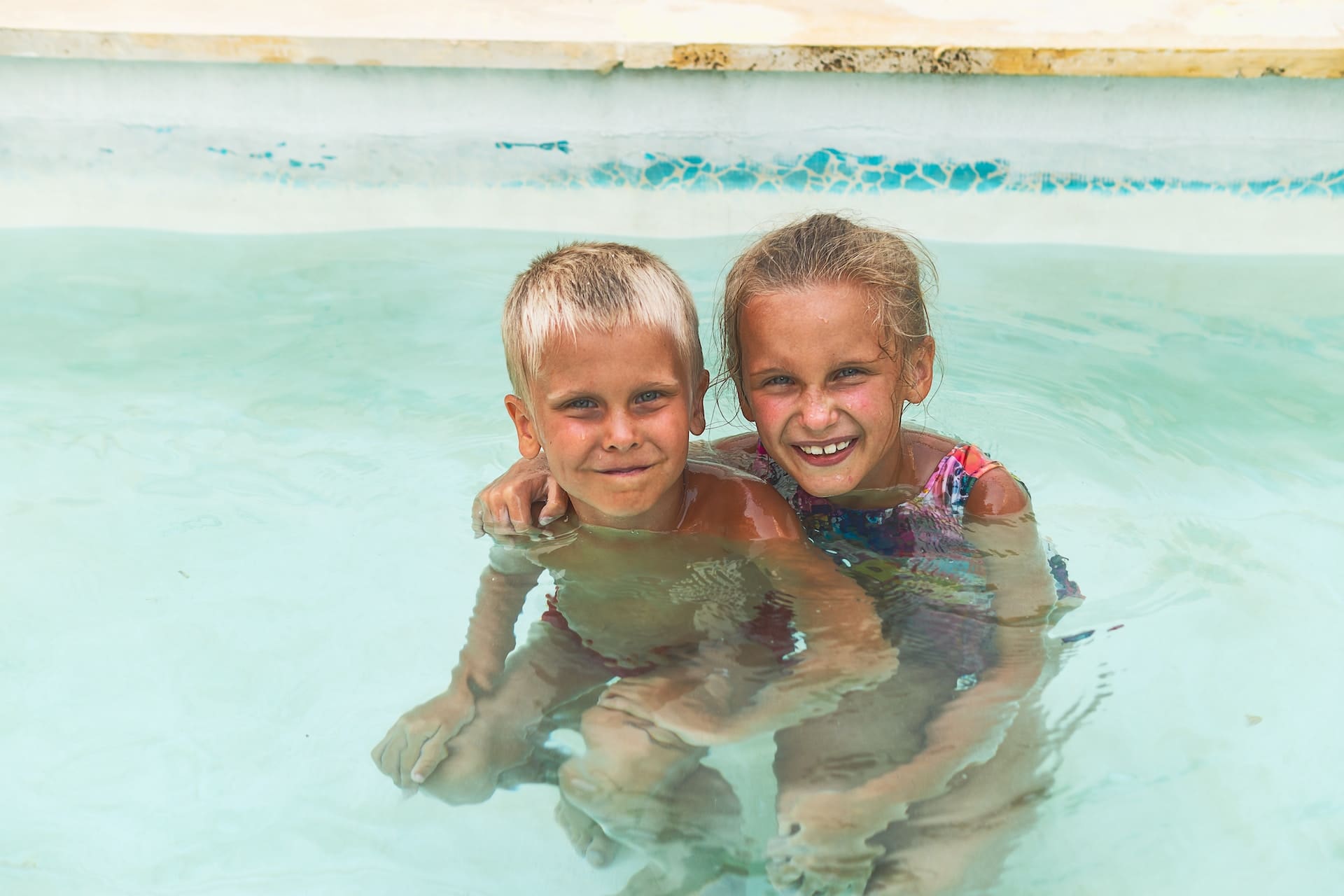 A modern backyard with a sleek swimming pool. Children splash and play, while adults lounge poolside, sipping from glasses filled with clear, chilled water garnished with berry slices.